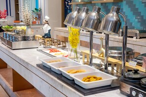 Montaje de bufé con varios recipientes de comida, una figurita de chef y un jarrón decorativo.