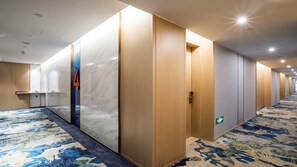 Un pasillo de hotel con pared de mármol, puertas de madera y alfombra estampada.
