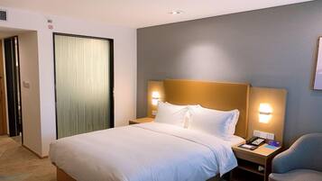 Una habitación de hotel con cama, lámparas de noche, una silla y una puerta.