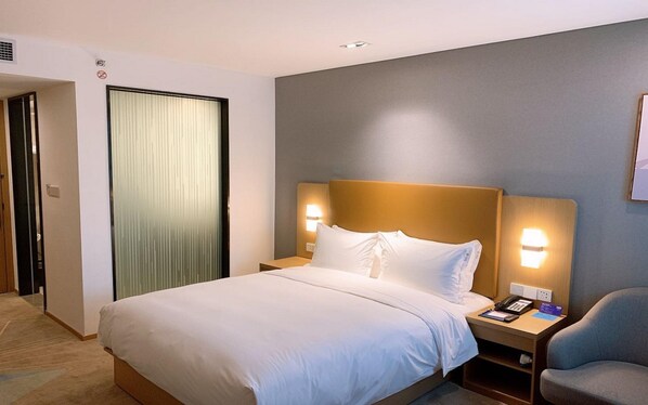 Una habitación de hotel con cama, lámparas de noche, una silla y una puerta.