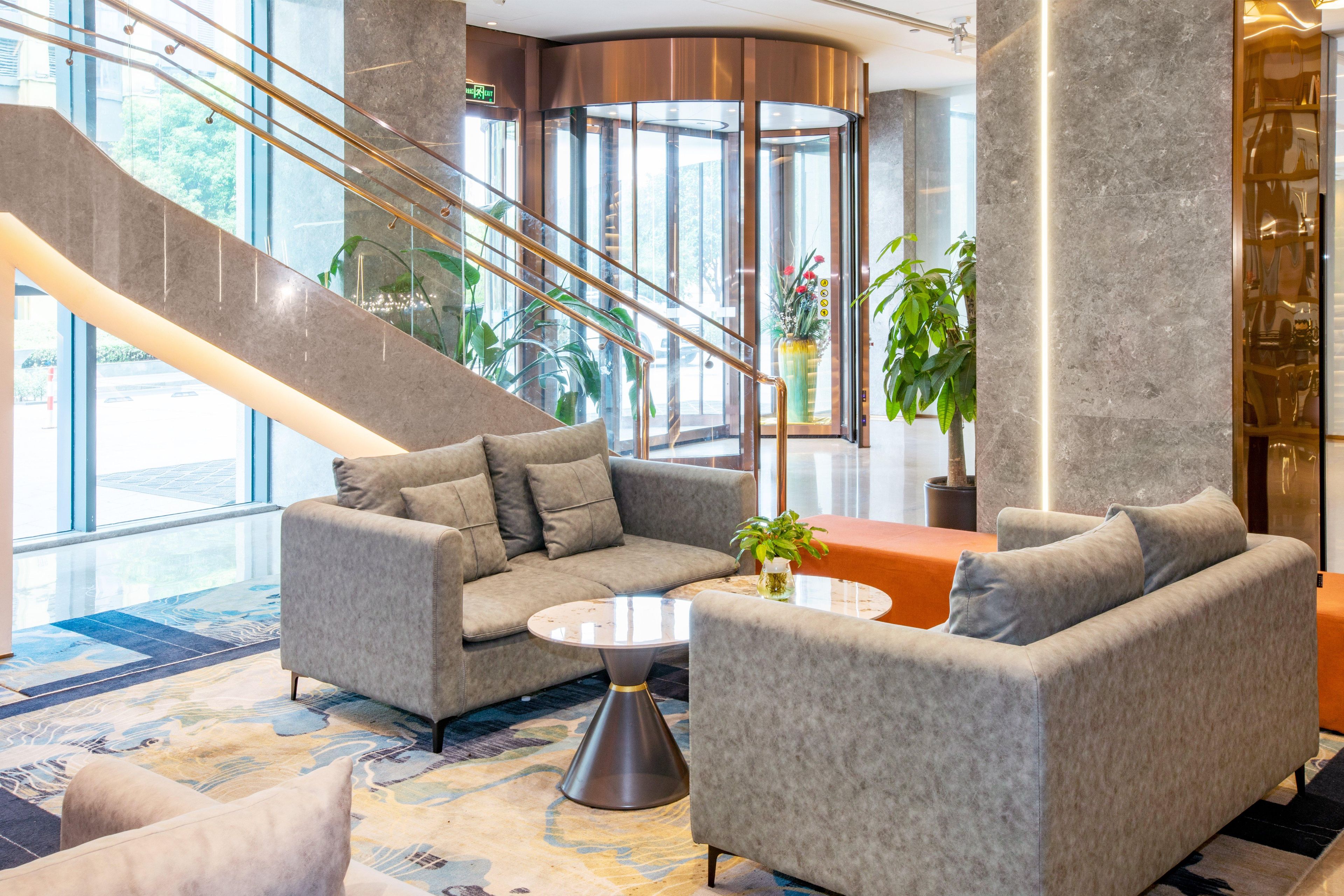 A lobby with a staircase, a sofa, a coffee table, and potted plants.
