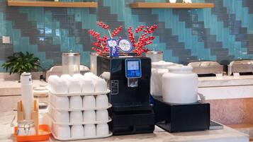 A coffee station with a water dispenser, stacks of disposable cups, and a decorative plant.