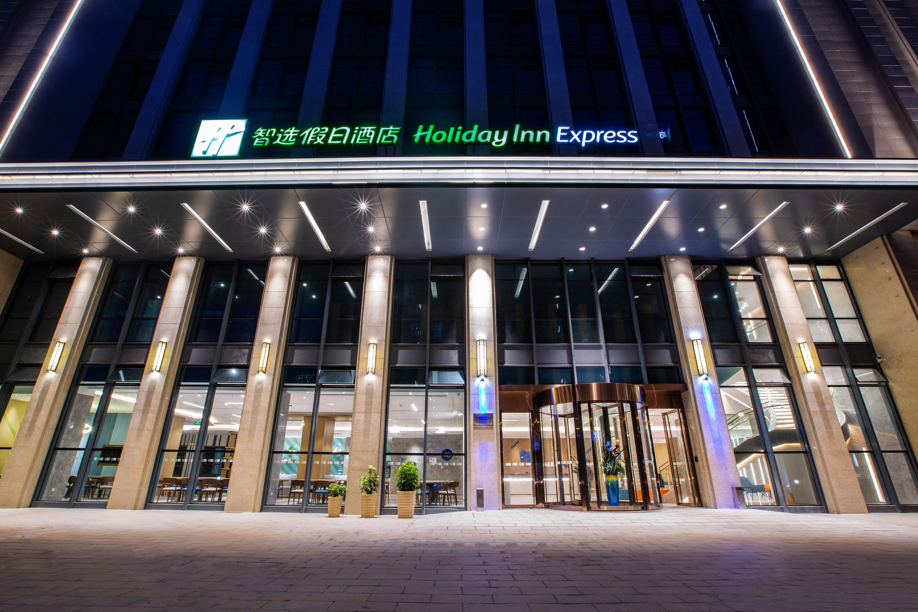 Un bâtiment de la chaîne Holiday Inn Express, doté d’une façade moderne, de grandes fenêtres en verre et d’une entrée bien visible.