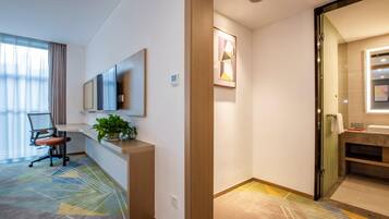 Habitación de hotel con escritorio, silla, planta en maceta y un ventanal con cortinas.