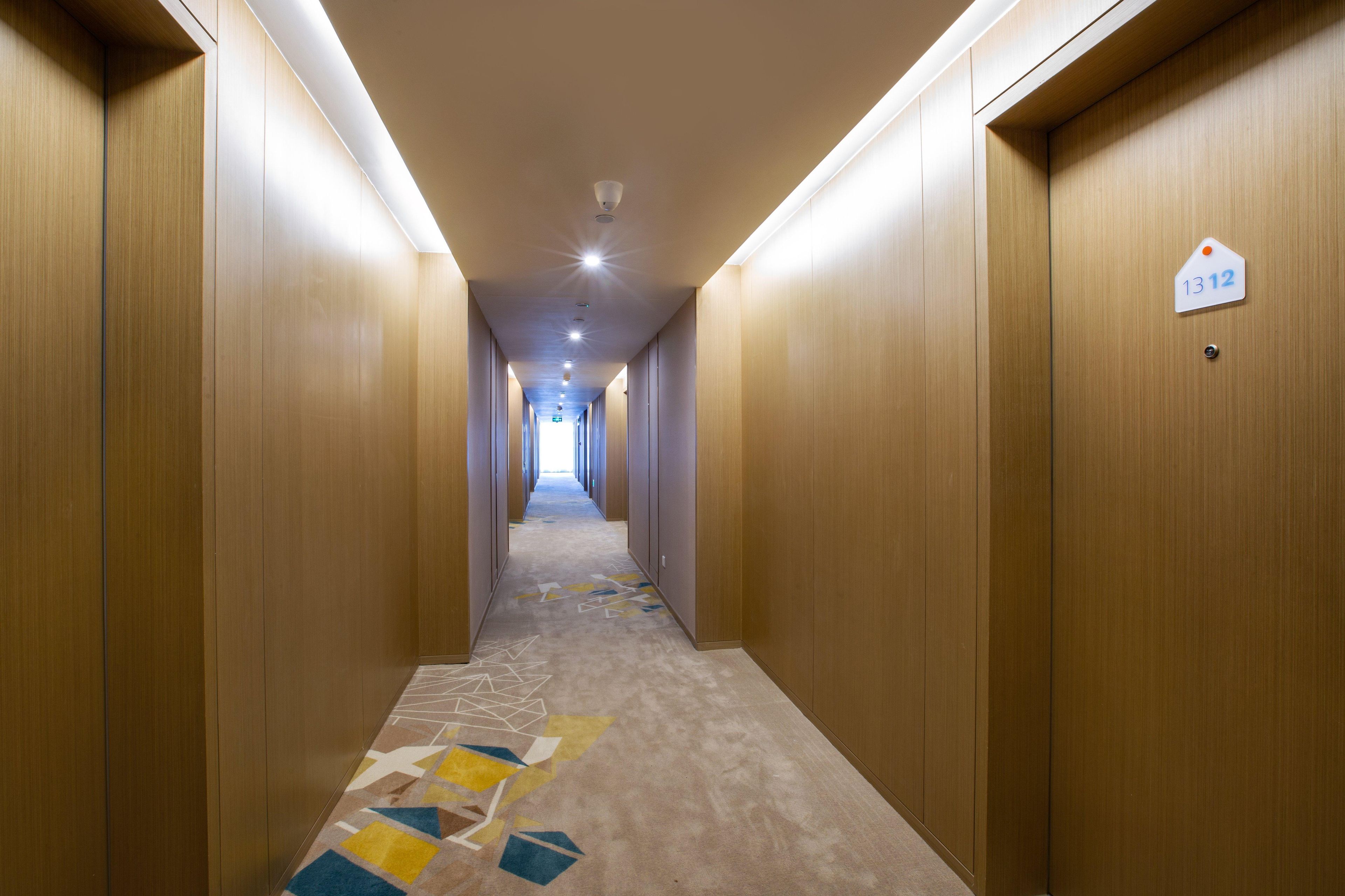 A hotel hallway with wooden walls, a carpeted floor with geometric patterns, and a sign indicating room number 1312.