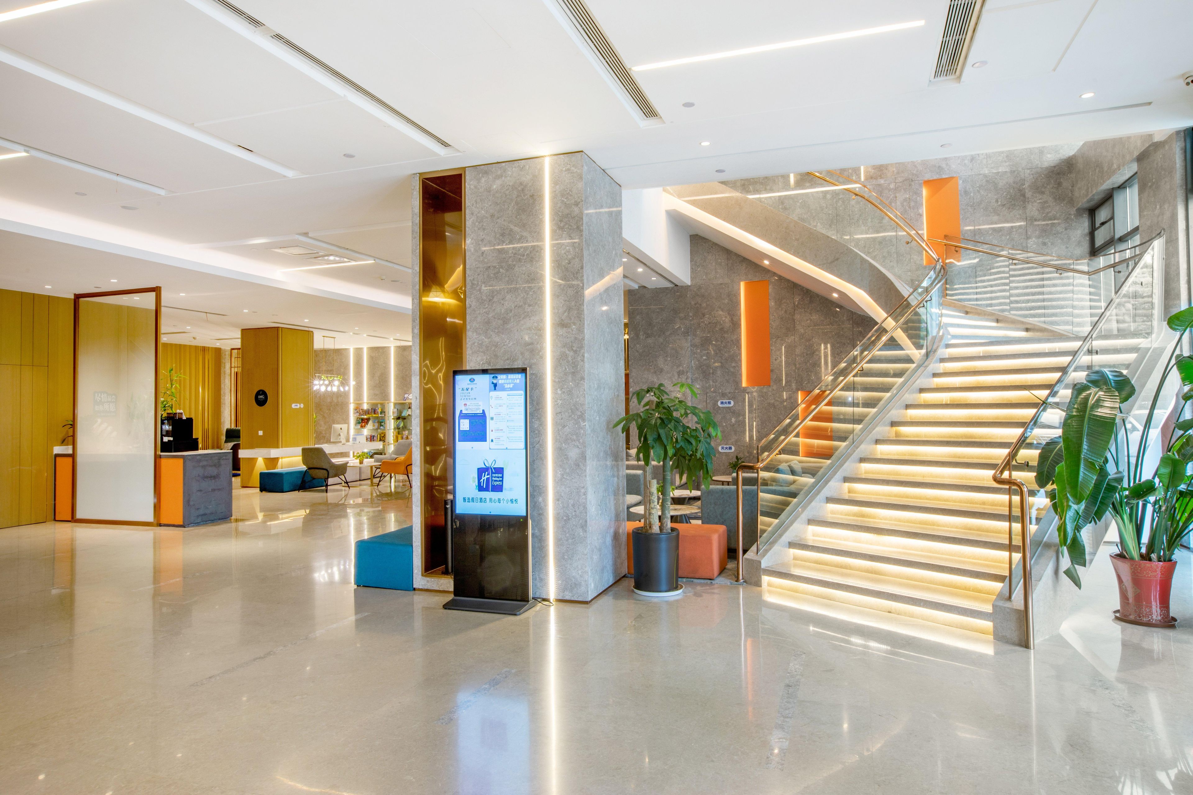 Een moderne lobby met een receptiebalie, zithoek en een trap.