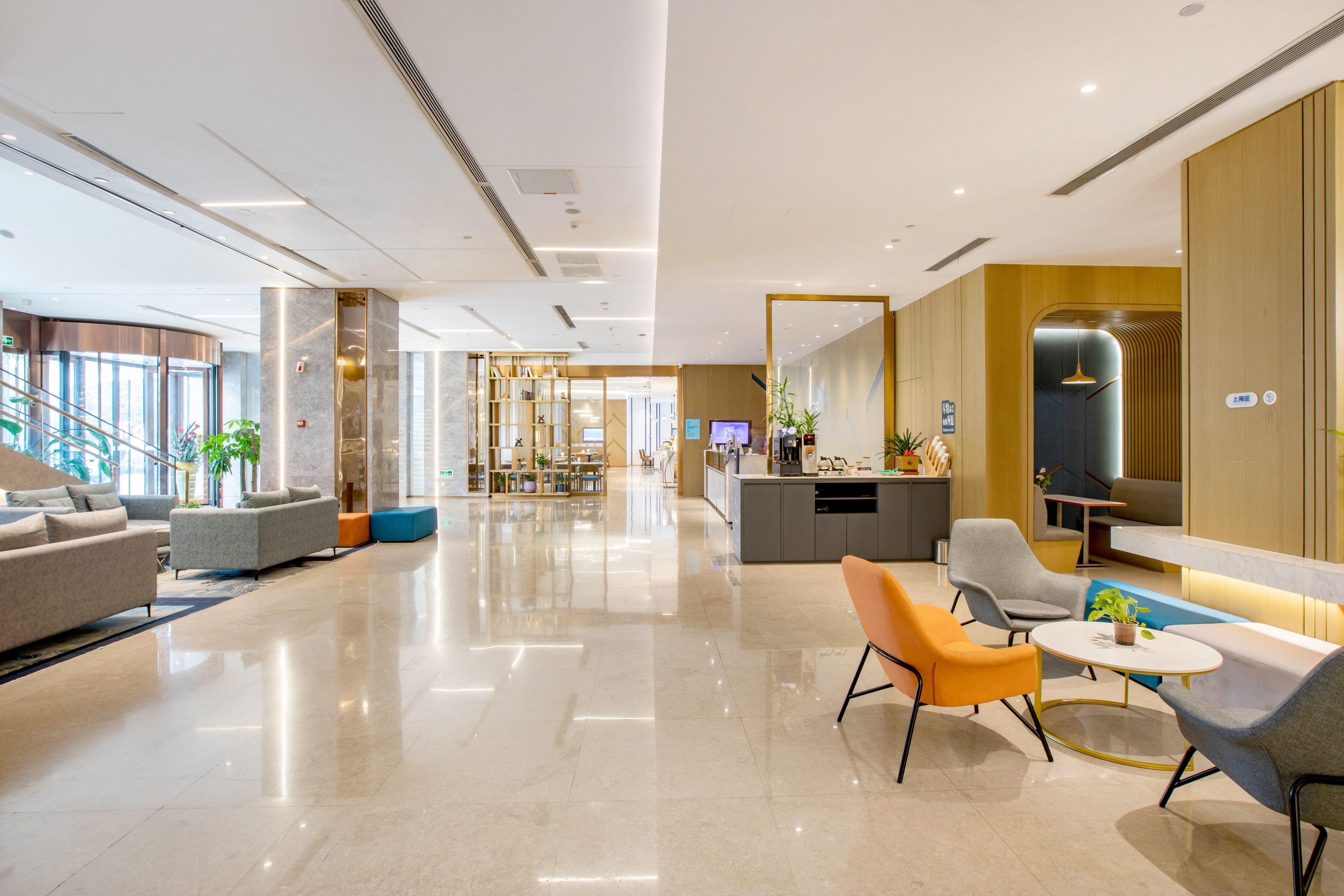 Een moderne hotellobby met een receptiebalie, een zithoek en een trap naar de andere verdiepingen.