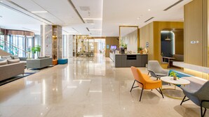 Un moderno vestíbulo de hotel con mostrador de recepción, zona de estar y una escalera que conduce a otras plantas.