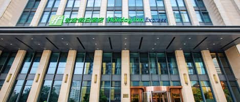Un edificio moderno con fachada de vidrio, un cartel llamativo de Holiday Inn Express y un conjunto de puertas dobles en la entrada.