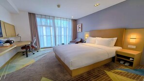 Habitación de hotel con cama, escritorio, silla y un ventanal con cortinas.