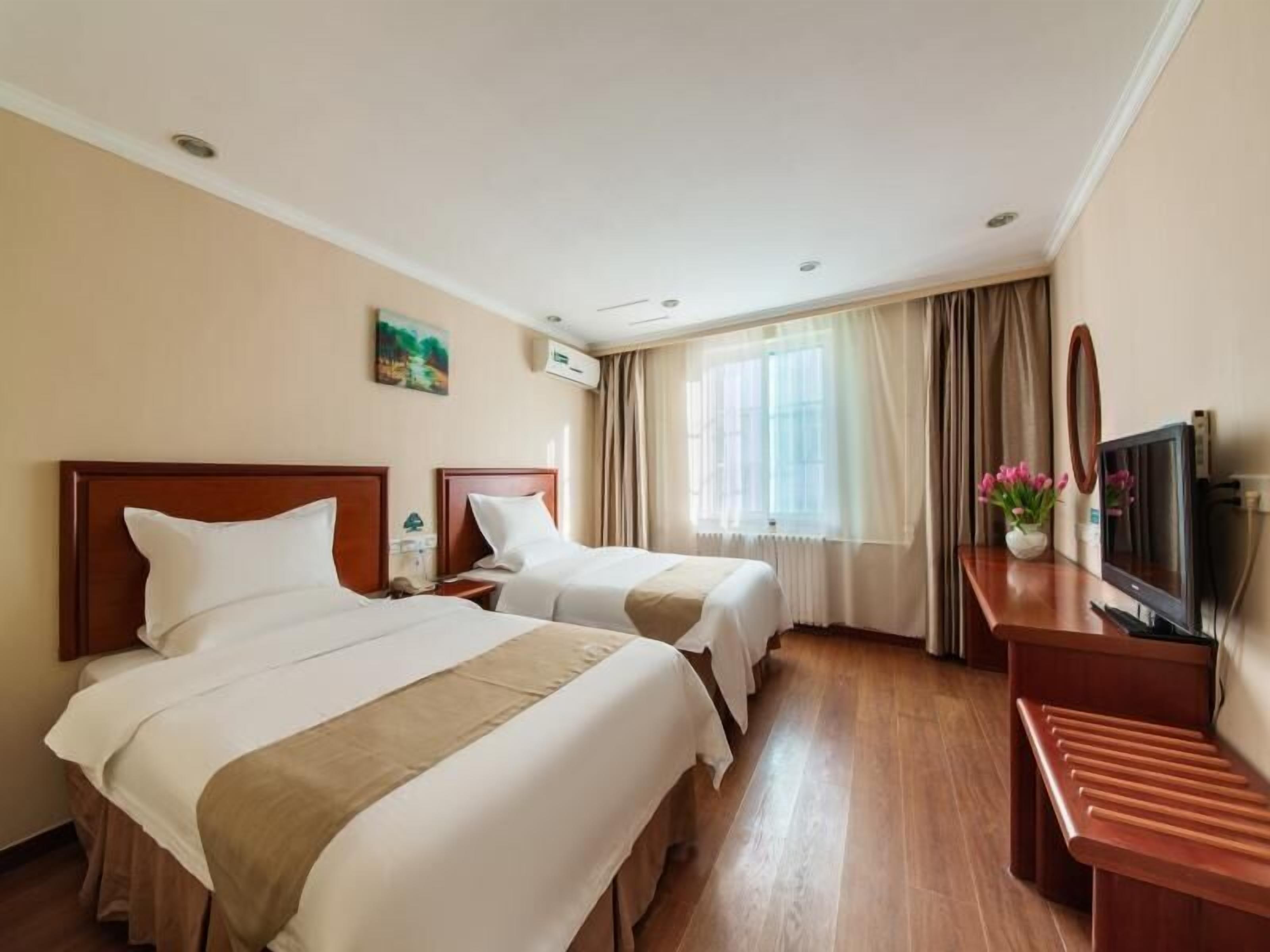 A hotel room with two beds, a wooden desk with a TV, a window with curtains, and a painting on the wall.