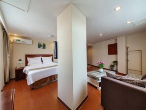 A hotel room with a bed, a desk with a lamp, a chair, a small table with flowers, and a coat rack. - Greentree Inn Liaocheng Gaotang Tianqi Temple Business Center Express Hotel (Liaocheng)