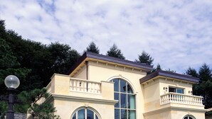 A two-story house with a large arched window, a balcony with balustrades, and a stone facade. - Crystal Valley CC - Golden Village (Gapyeong)
