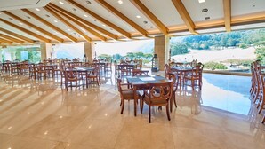 A spacious dining area with wooden tables and chairs, large windows offering a view of a beach and mountains. - Crystal Valley CC - Golden Village (Gapyeong)