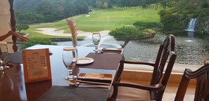 A dining table set with a menu, a glass, and cutlery, overlooking a golf course and a waterfall. - Crystal Valley CC - Golden Village (Gapyeong)