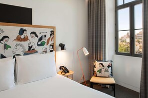 A hotel room with a bed, a chair with a cushion, a bedside table with a lamp, a phone, and a wall with a mural. - Se Catedral Hotel Porto, Tapestry Collection by Hi (Porto)