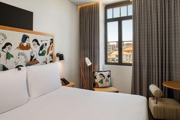 Quarto de hotel com cama, cadeira, mesa, luminária e um quadro na parede.