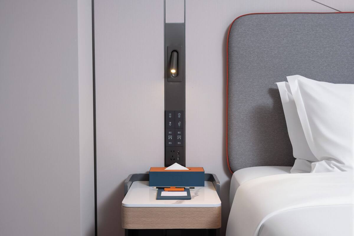 Een hotelkamer met een bed, nachtkastje en een bedieningspaneel aan de muur.