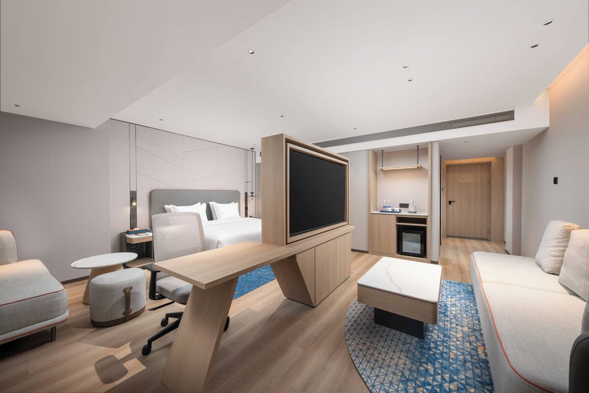 Een moderne hotelkamer met een bed, een televisie, een bureau, een bank, een klein tafeltje en een badkamer die door een open deur zichtbaar is.