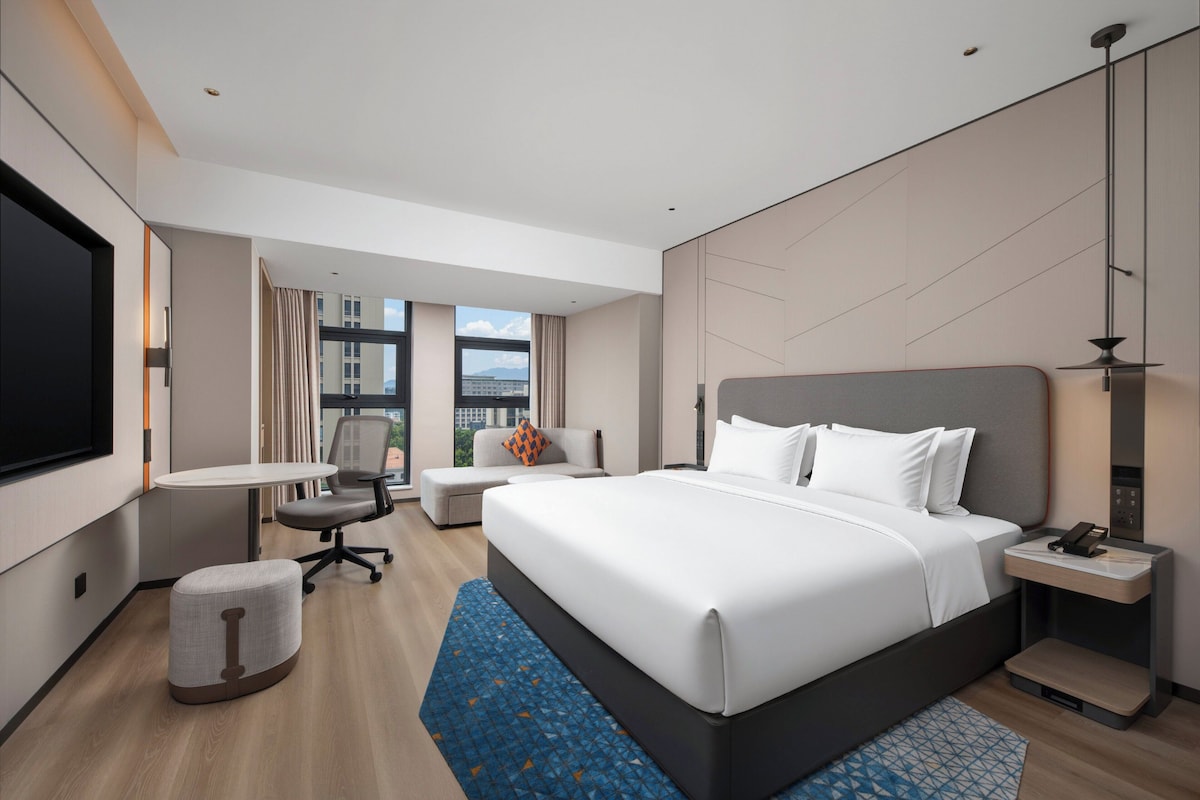 A modern hotel room with a large bed, a desk, a chair, and a TV.