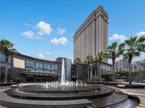 A modern building with a fountain, palm trees, and a clear blue sky.