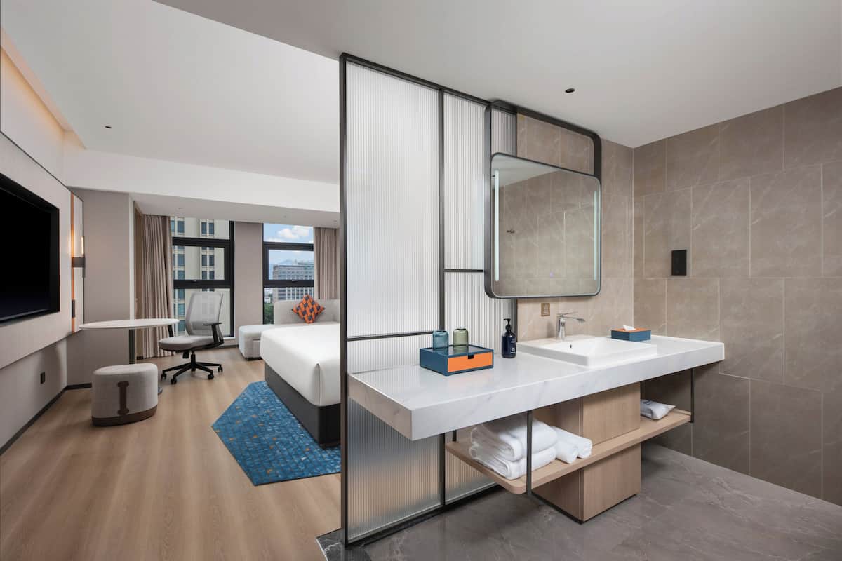 Een moderne hotelkamer met een groot bed, een bureau, een stoel, een badkamer met spiegel en uitzicht op de stad.
