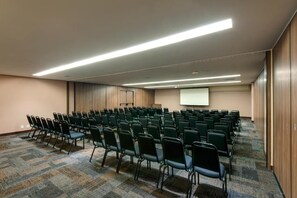 A conference room with rows of chairs, a projector screen, and a carpeted floor. - Denali Hotel (Anapolis)