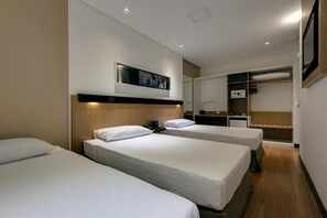 A hotel room with three single beds, a wooden headboard, a flat-screen TV, a wardrobe, and a small desk with a chair. - Denali Hotel (Anapolis)