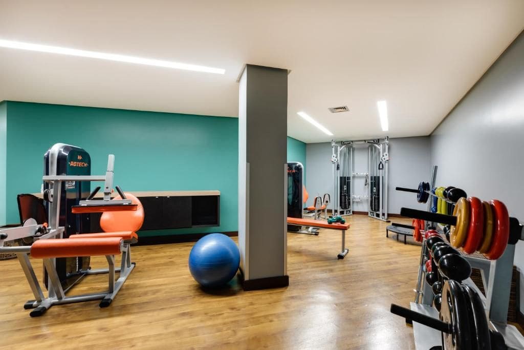 Un gimnasio con equipo de ejercicio, una pelota azul de ejercicio y jaulas para levantamiento de pesas.