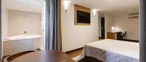 A hotel room with a bed, a desk, a chair, a TV mounted on the wall, and a bathroom with a bathtub.