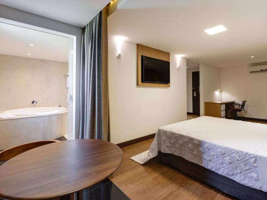 Habitación de hotel con cama, escritorio, silla, televisor montado en la pared y baño con bañera.