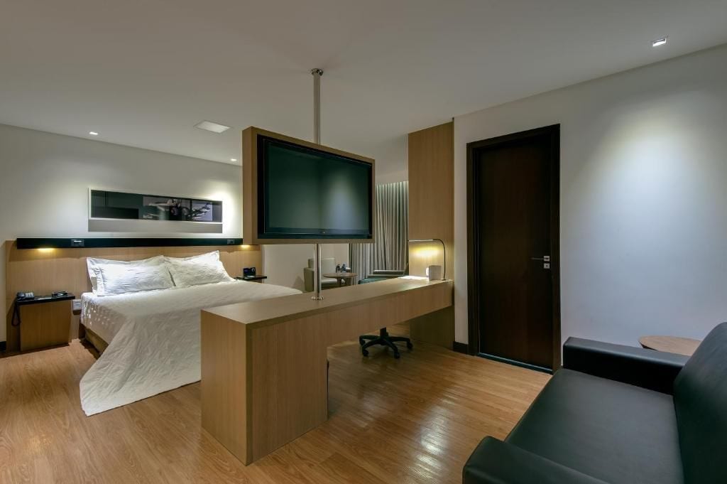 A modern hotel room with a bed, desk, TV, and a sofa.