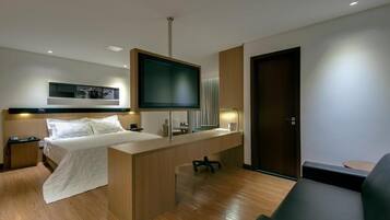 A modern hotel room with a bed, desk, TV, and a sofa.