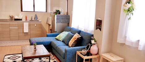 A modern living room with a blue sofa, a patterned rug, a wooden coffee table, and a small wooden side table with a vase.