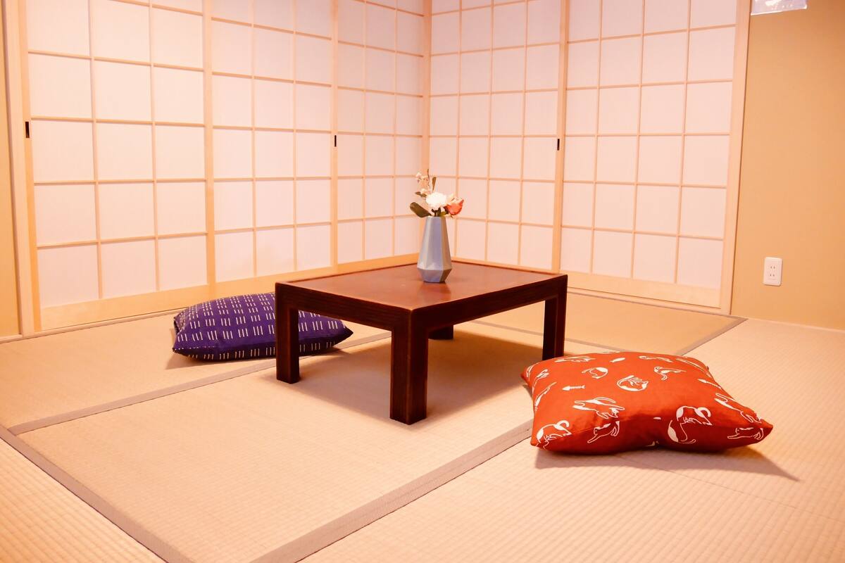 A tatami mat room with a low wooden table, a vase with flowers, and two cushions.