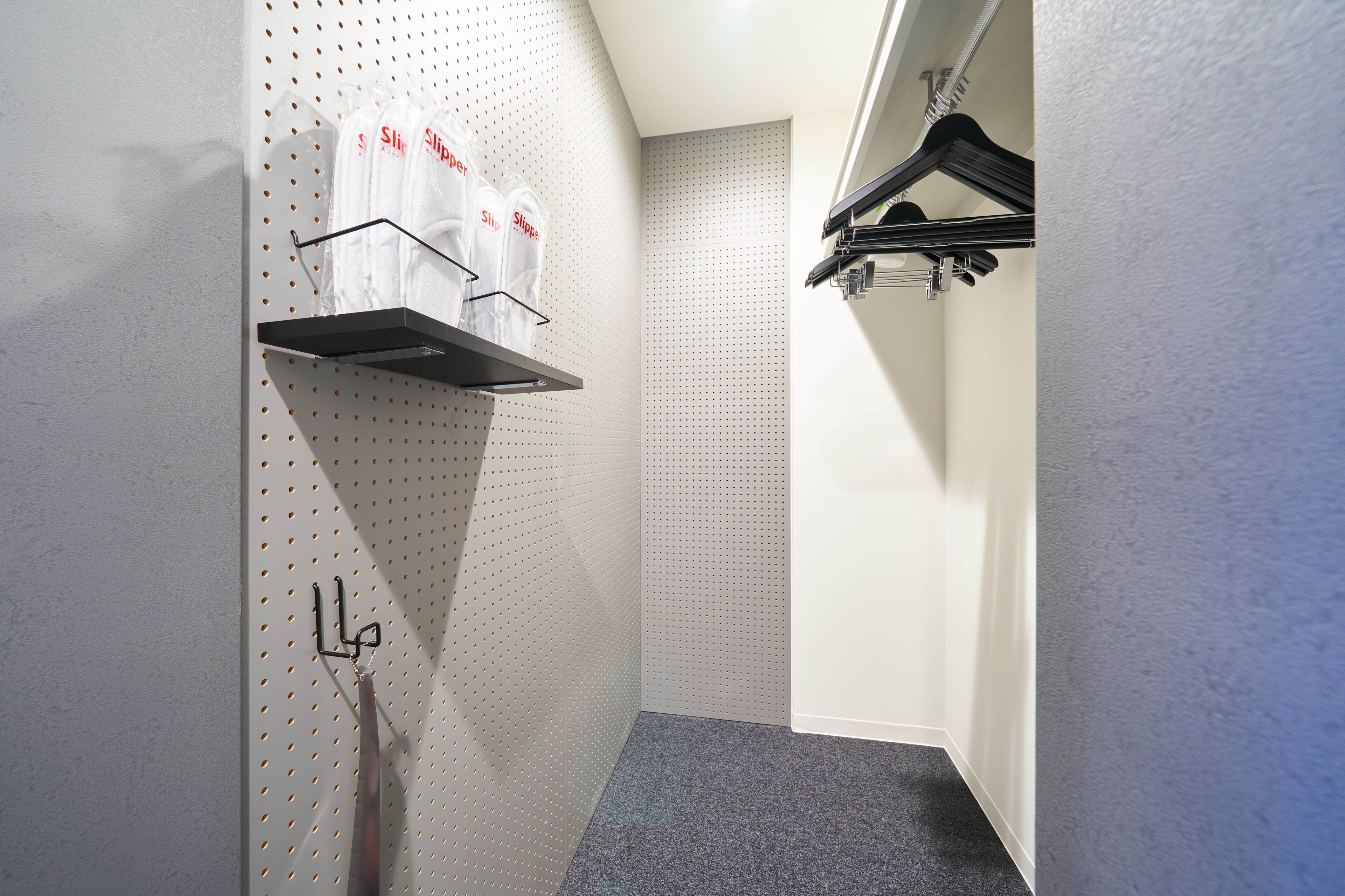 A hotel room with a pegboard wall, a shelf with bags, and a coat rack.