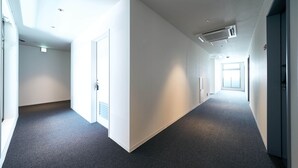 A long, narrow hallway with white walls and a dark carpet. There are doors on both sides, and the hallway leads to a bright area at the end. - Rakuten STAY Osaka Station North (Osaka)
