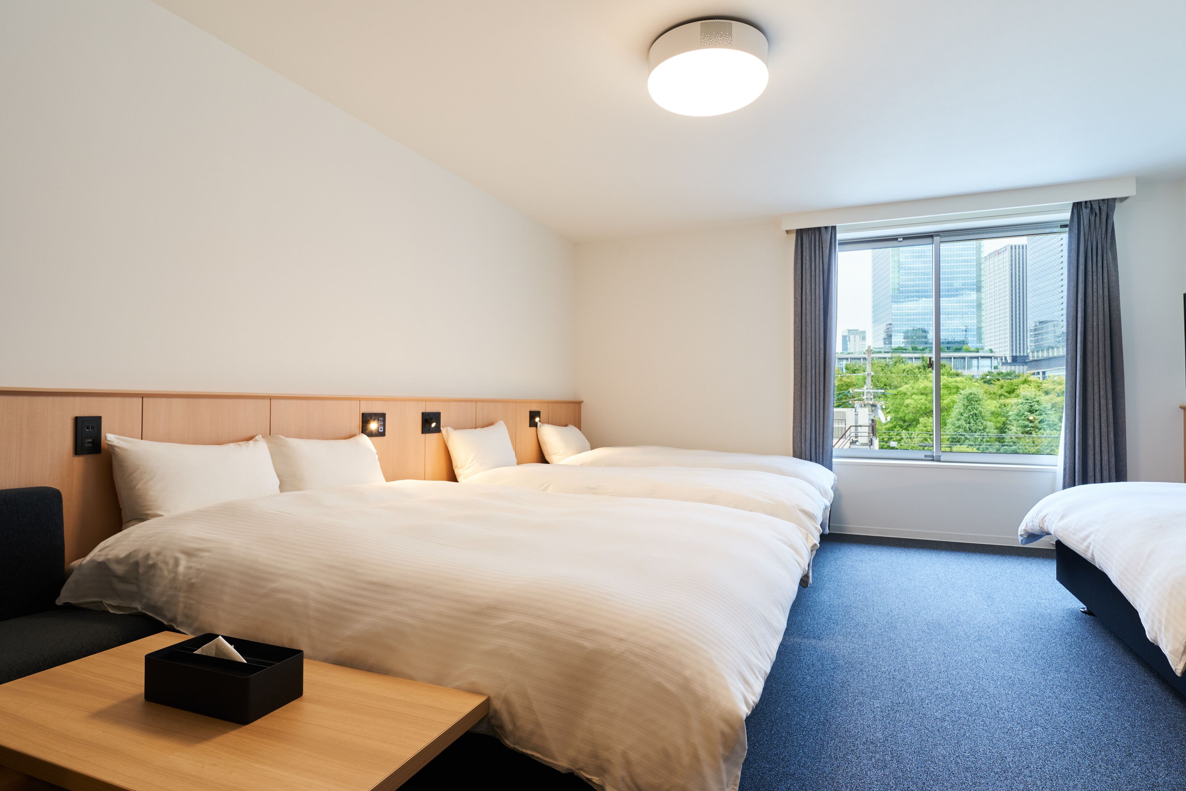 A hotel room with a large bed, a desk, and a view of the city through the window.