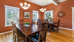 A dining room with a large wooden table, six chairs, two chandeliers, and large windows with white frames. - Royal Oak Manor Lrg private home and yard sleeps 18! (Bend)