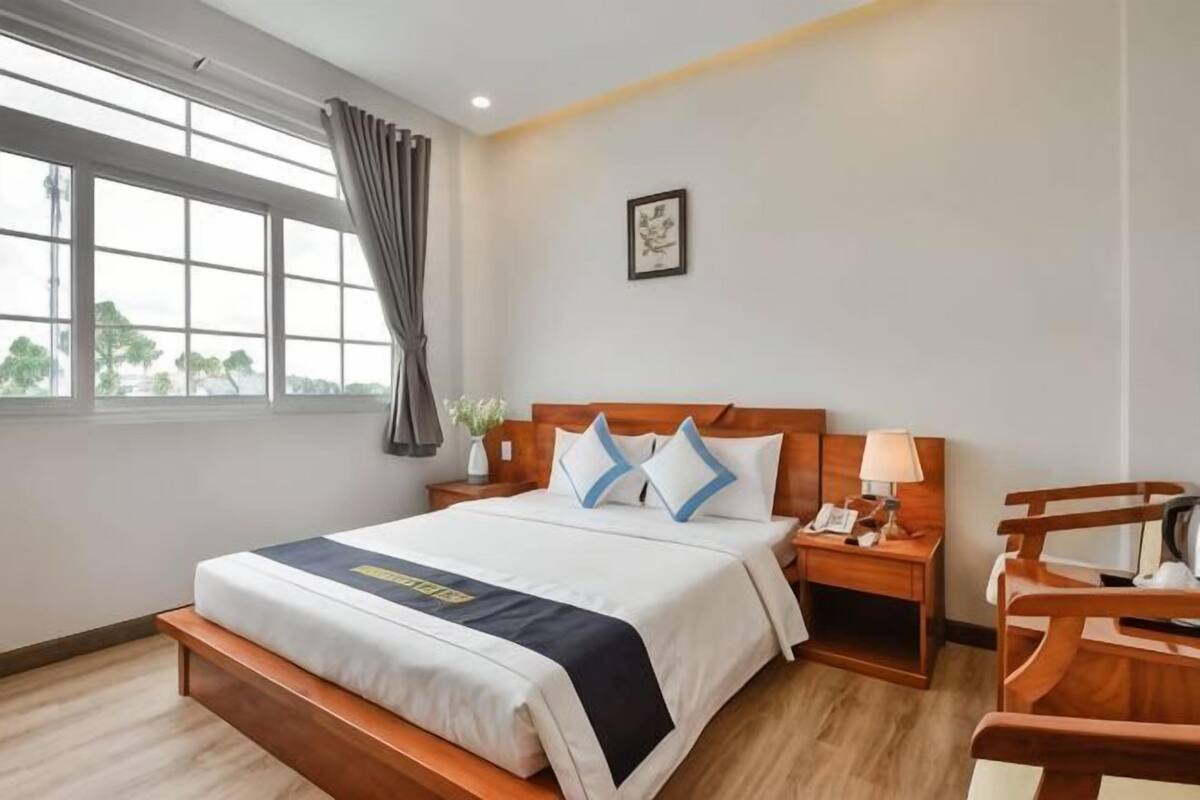 Habitación de hotel con cama, mesita de noche, lámpara, silla y ventana con cortinas.