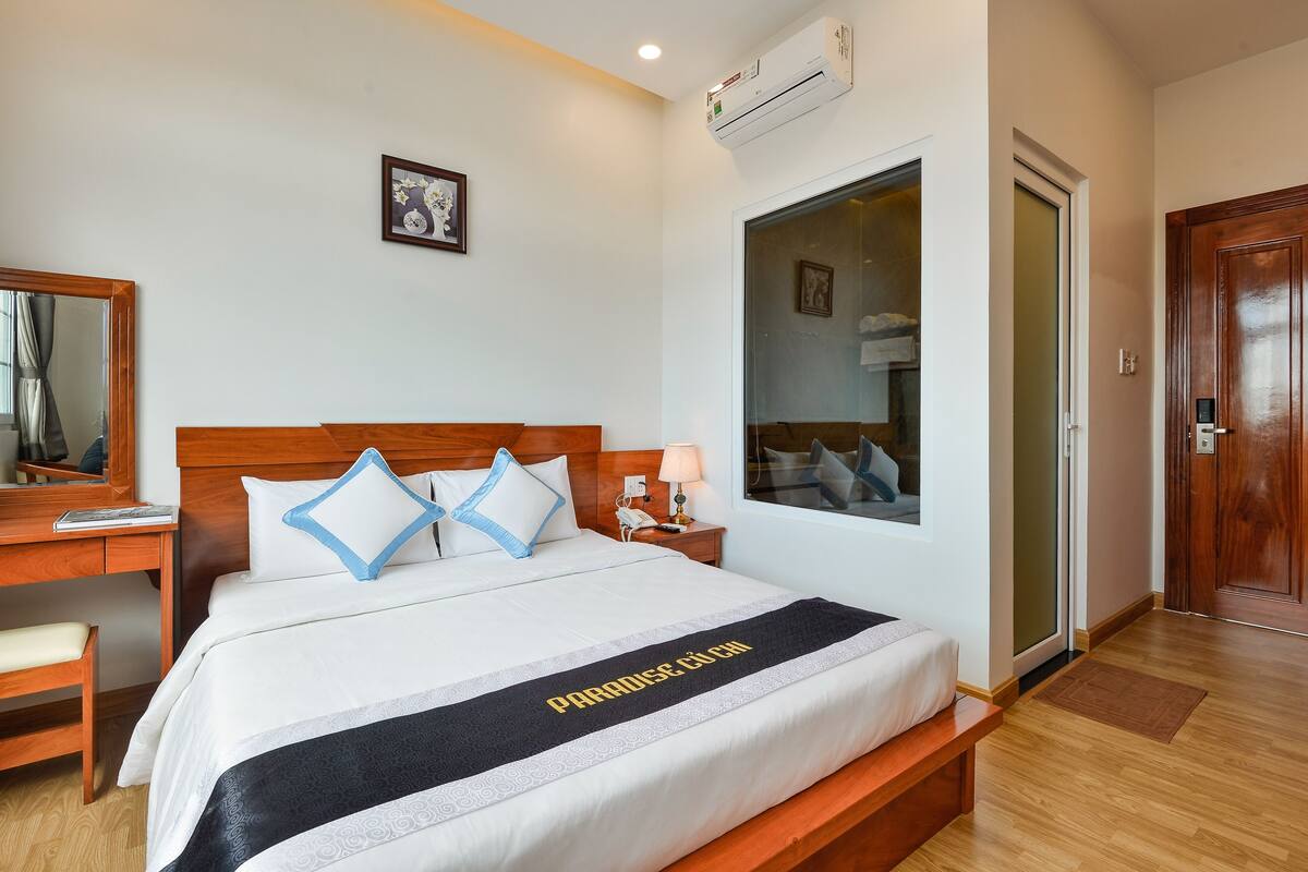 Habitación de hotel con cama, escritorio, silla, ventana y aire acondicionado.