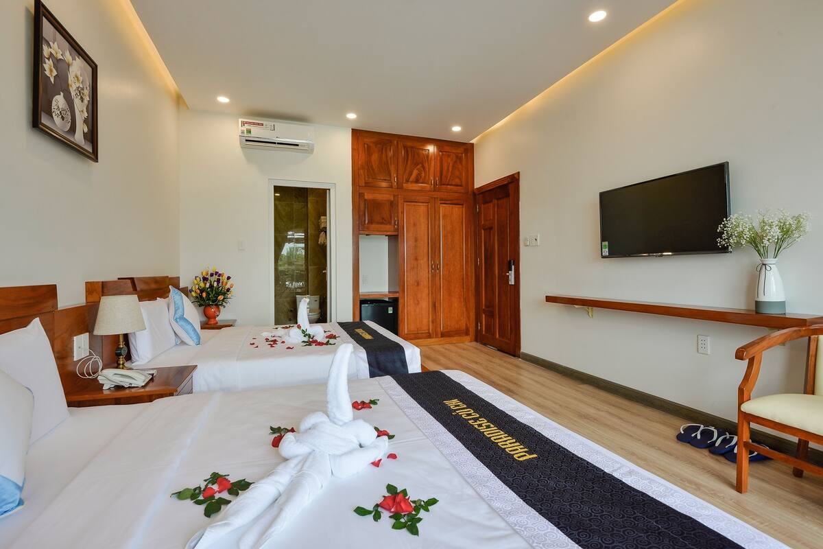 Habitación de hotel con dos camas, televisor, armarios de madera y zona de ducha.