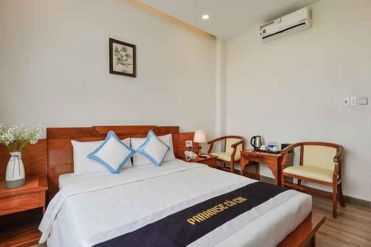 A hotel room with a bed, a desk, a chair, and a bedside table.