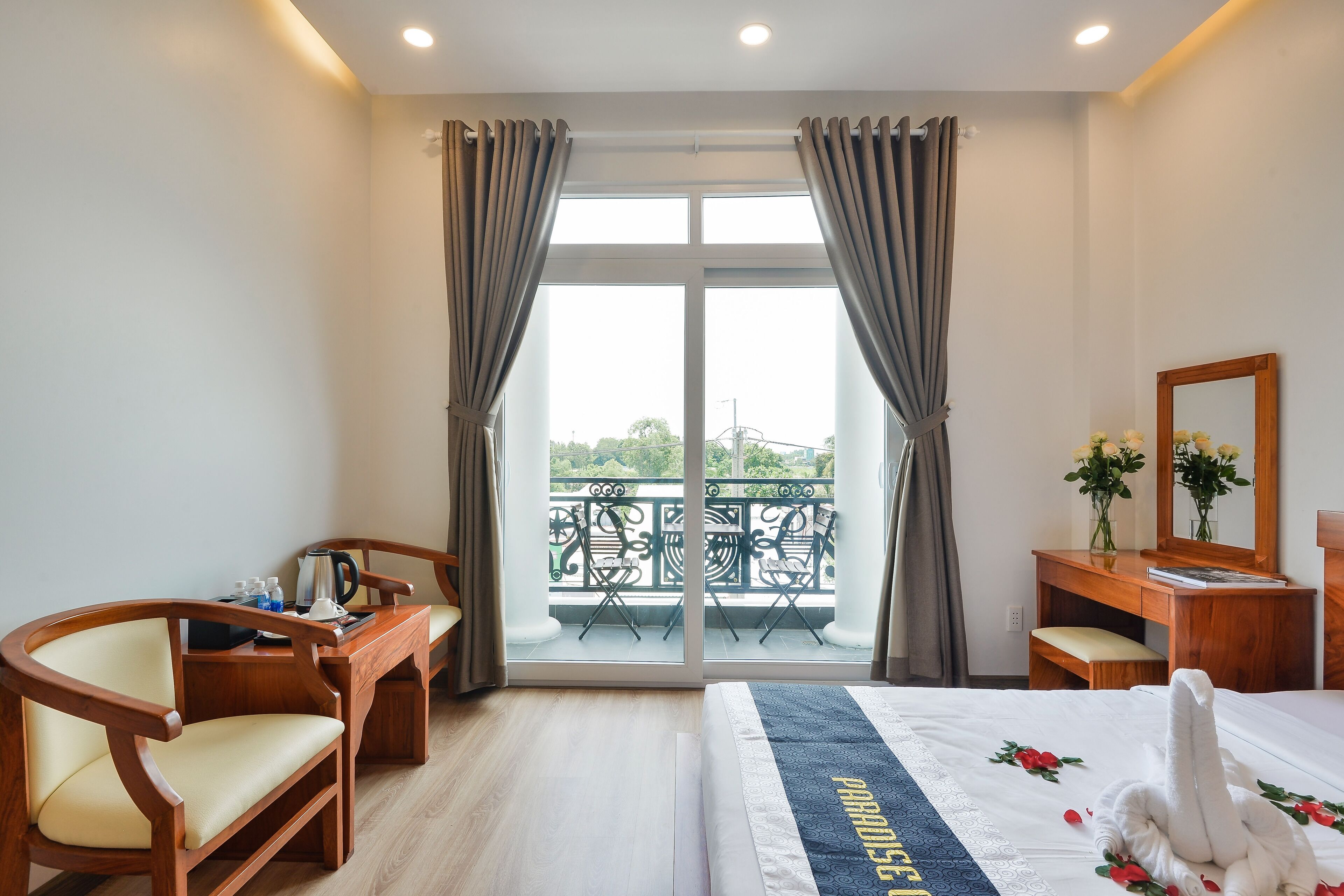 Habitación de hotel con cama, escritorio de madera, sillas, balcón con vistas y espejo.