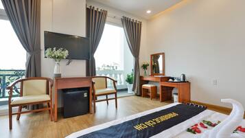 A hotel room with a bed, desk, chairs, a TV, and a balcony view.