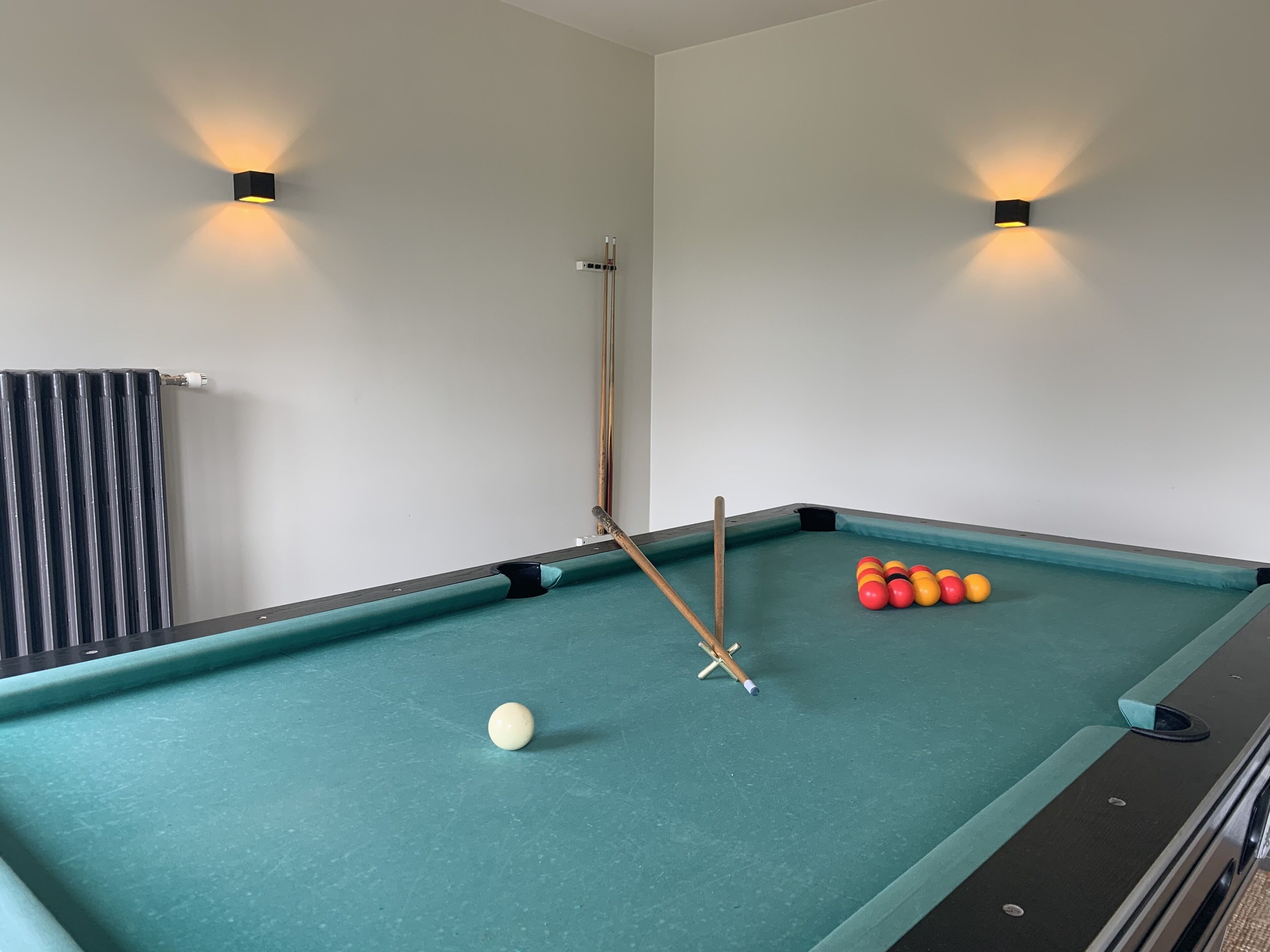 Una mesa de billar con bolas y tacos, un radiador, y luces fijadas en la pared.