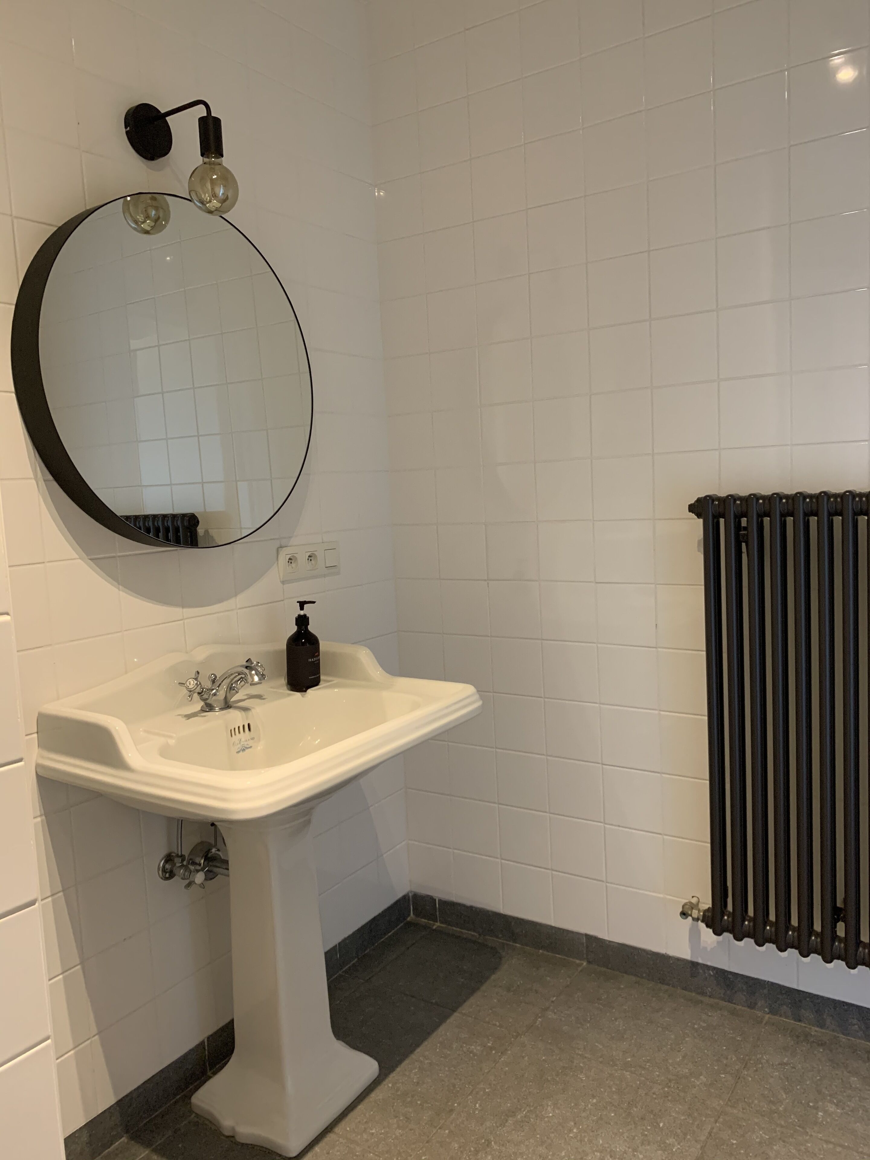 A bathroom with a white sink, a round mirror, and a black radiator.