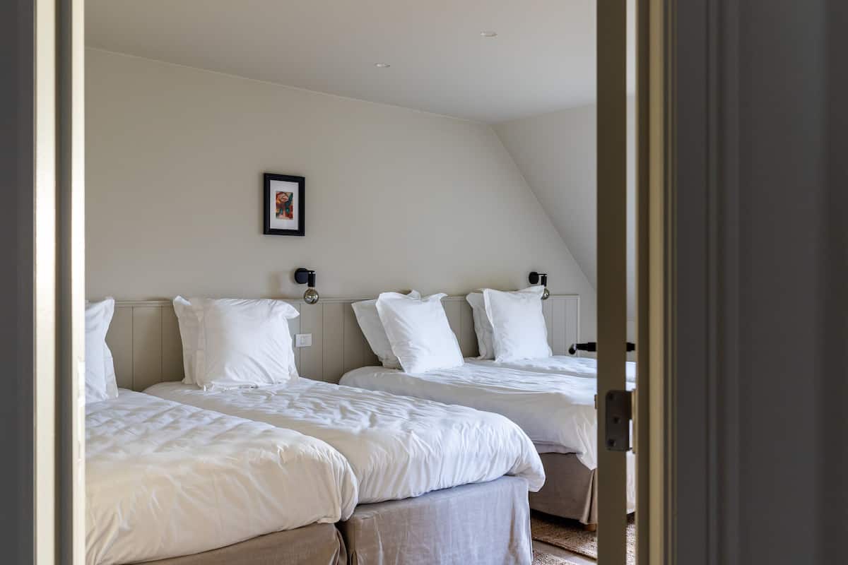 A bedroom with two beds, a framed picture on the wall, and a door leading to another room.