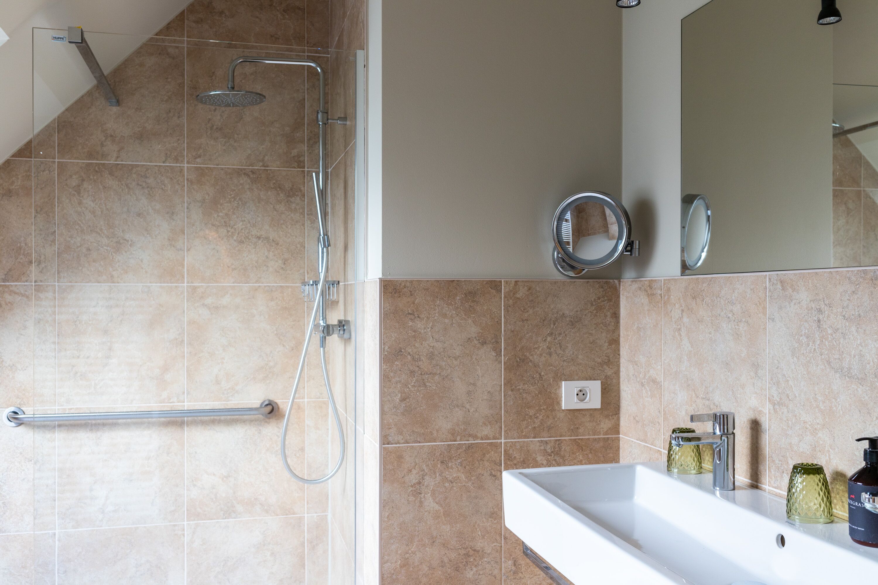 A bathroom with a shower, a handrail, a sink, and a mirror.