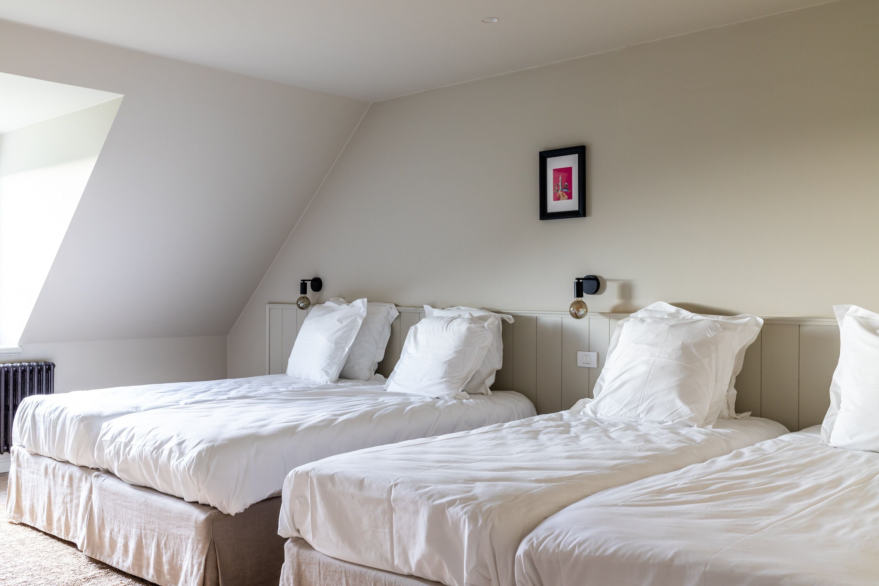 Una habitación con dos camas, un cuadro en la pared y un radiador.